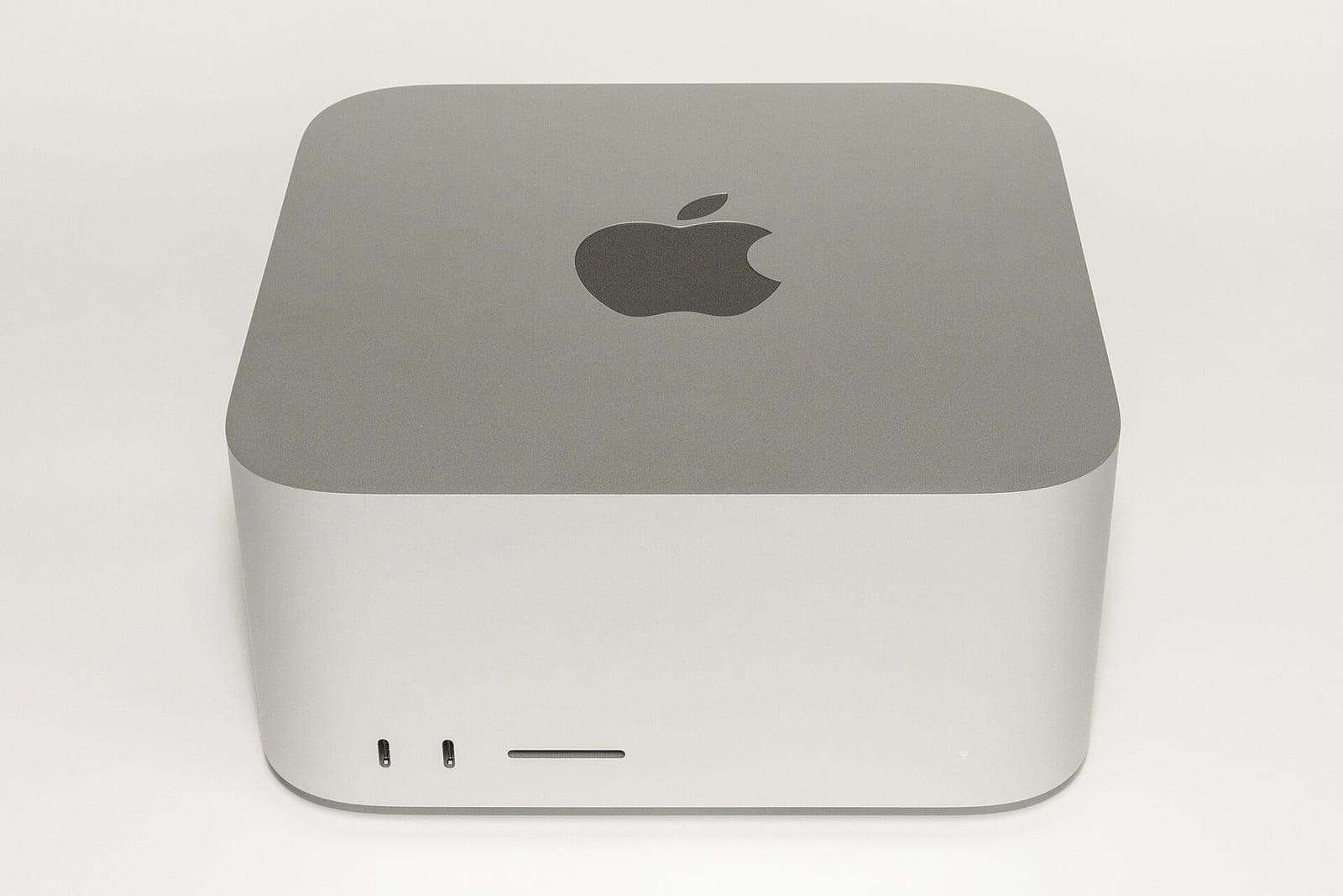 A silver Apple Mac Studio on a white surface, front ports facing the camera.